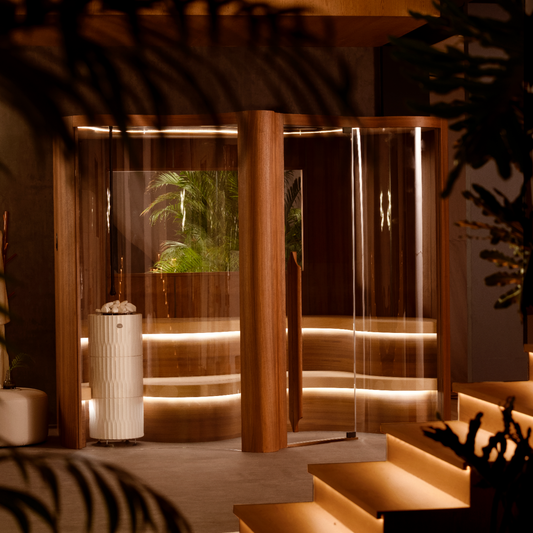 Modern indoor Sauna with glass enclosure and illuminated interior, surrounded by plants.