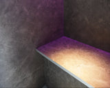 Corner of a steam room with textured walls and a lit shelf.