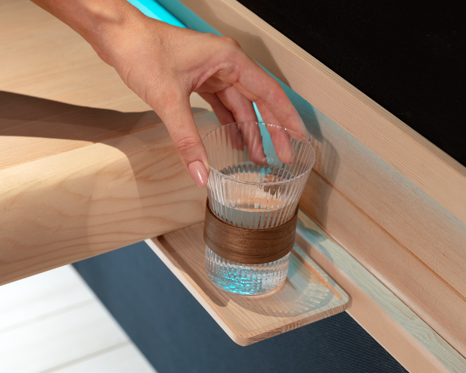 Hand reaching for a glass of water on a wooden tray in a sauna.